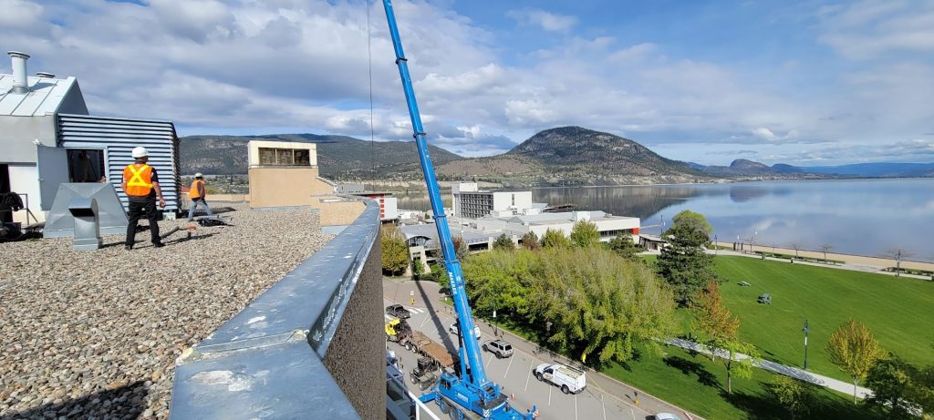 crane lifting materials to two workers standing on a roof
